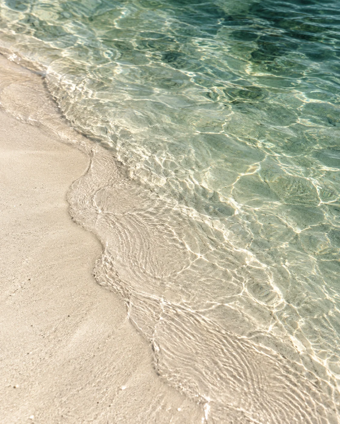 Sunlight on clear emerald water washing over pale sand